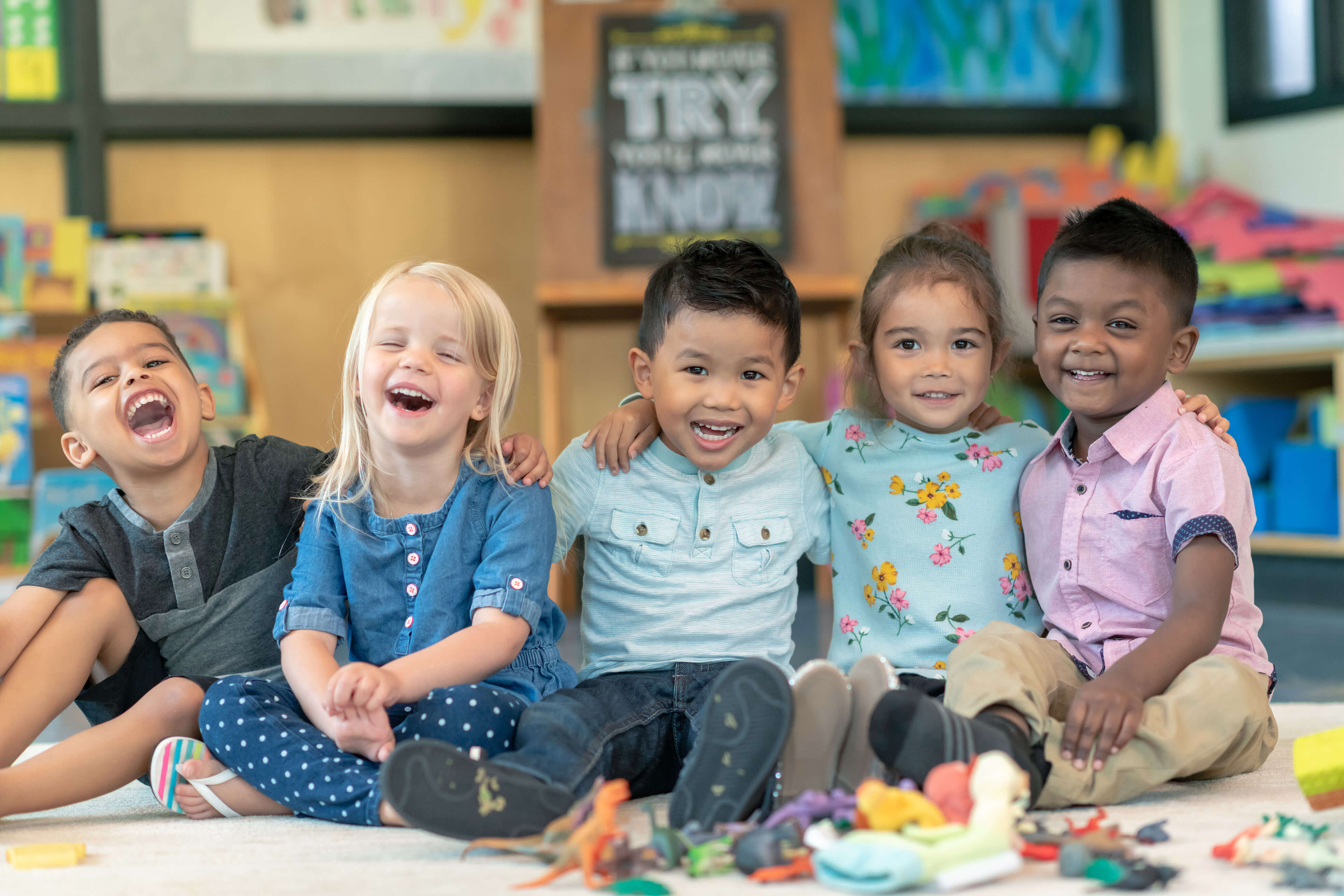 Cinco niños sentados en el suelo sonriendo y jugando con juguetes.